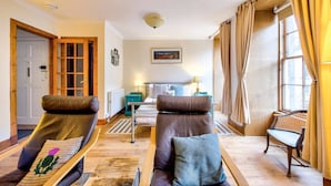Une pièce comprenant deux canapés en cuir, un lit, une fenêtre avec des rideaux, un radiateur et un tableau accroché au mur.