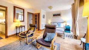 Une chambre d’hôtel avec un lit, deux fauteuils à bascule, une petite table, une lampe et une vue sur l’extérieur.