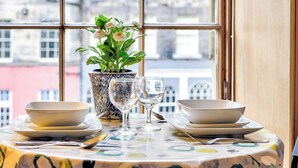 Une table à manger dressée avec des assiettes, des bols et des verres à vin, agrémentée d’une plante en pot et d’une nappe à motifs.