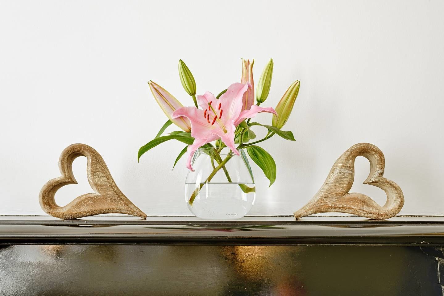 A vase with pink lilies on a shelf.