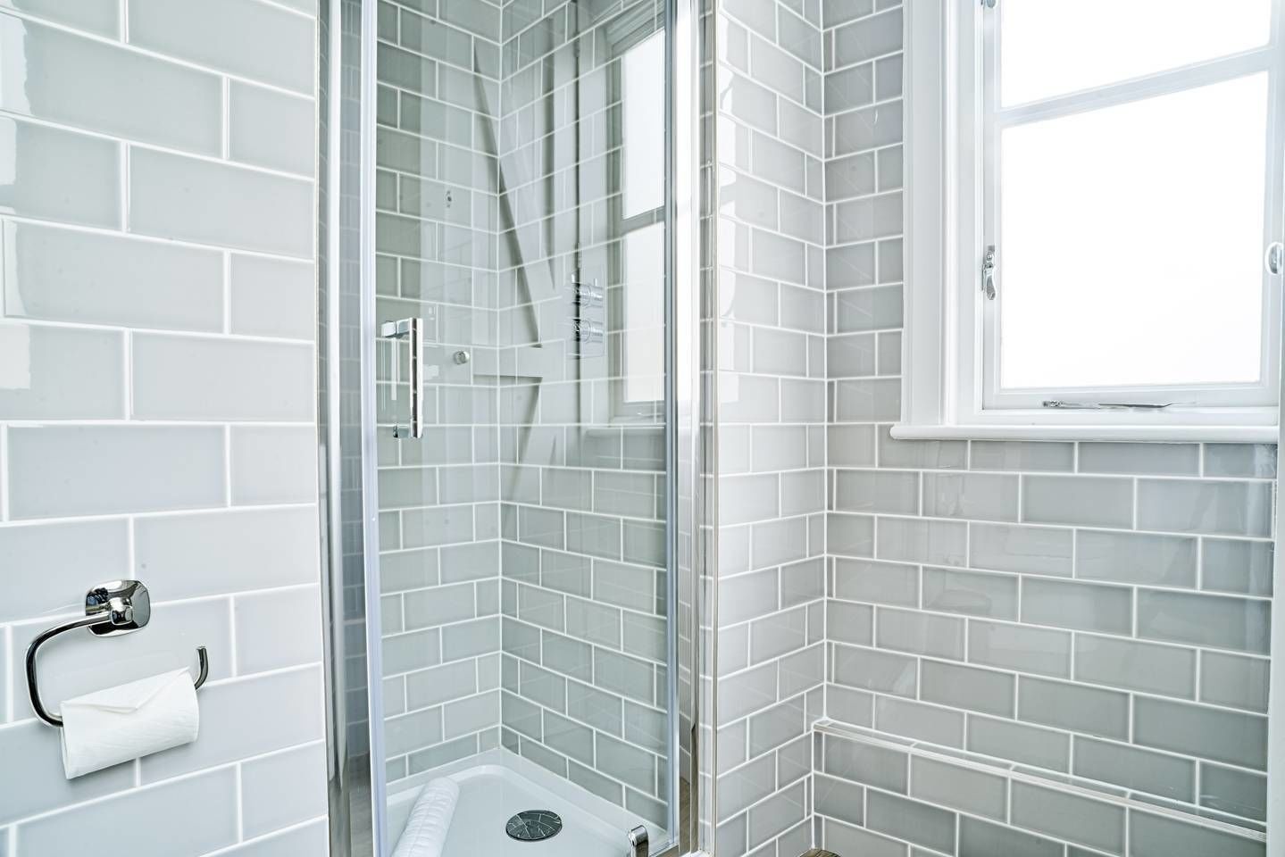 A modern bathroom with white subway tiles, a glass shower enclosure, and a window.
