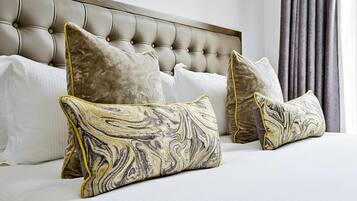 A bed with a tufted headboard, white linens, and decorative pillows with a marbled pattern.