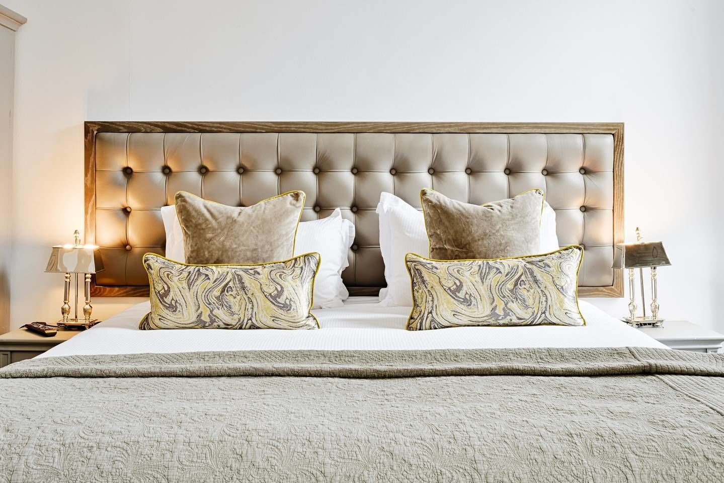 A bedroom with a tufted headboard, two matching pillows, a bedside table with a lamp, and a nightstand.
