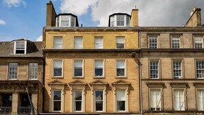 Une rangée d’immeubles à trois étages, tous dotés d’une conception uniforme de leurs fenêtres, et une section centrale qui se distingue par un élément architectural particulier.