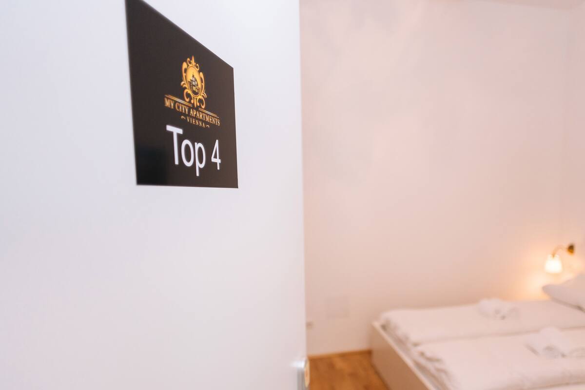 Une chambre d’hôtel avec un lit, une porte sur laquelle est apposée une pancarte indiquant qu’il s’agit d’un établissement classé parmi les « 4 meilleurs », et une clé accrochée à la porte.