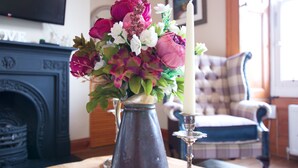 A vase with flowers on a table in a room with a fireplace and a plaid chair. - JOIVY Gorgeous Two Bedroom Apartment With Castle Views (Edinburgh)