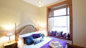 A neatly made bed with a headboard, a window seat with cushions, and two bedside lamps. - JOIVY Gorgeous Two Bedroom Apartment With Castle Views (Edinburgh)