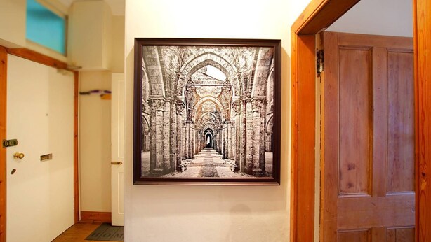 A hallway with a framed photograph of an ancient stone structure. - JOIVY Gorgeous Two Bedroom Apartment With Castle Views (Edinburgh)