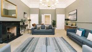 A spacious living room with a fireplace, a sofa, a dining area, and a chandelier. - JOIVY Palmerston Place Residence: Luxury City Centre Apt With Private Parking (Edinburgh)