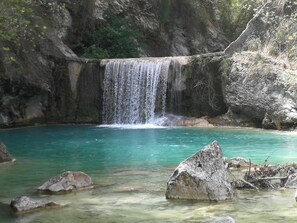 Una cascada se precipita en una piscina turquesa cristalina rodeada de rocas y follaje.