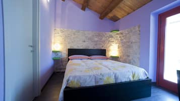 Una camera da letto con parete in pietra, soffitto in legno e un letto con copripiumino floreale.