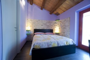 Un dormitorio con pared de piedra, techo de madera y cama con colcha estampada.
