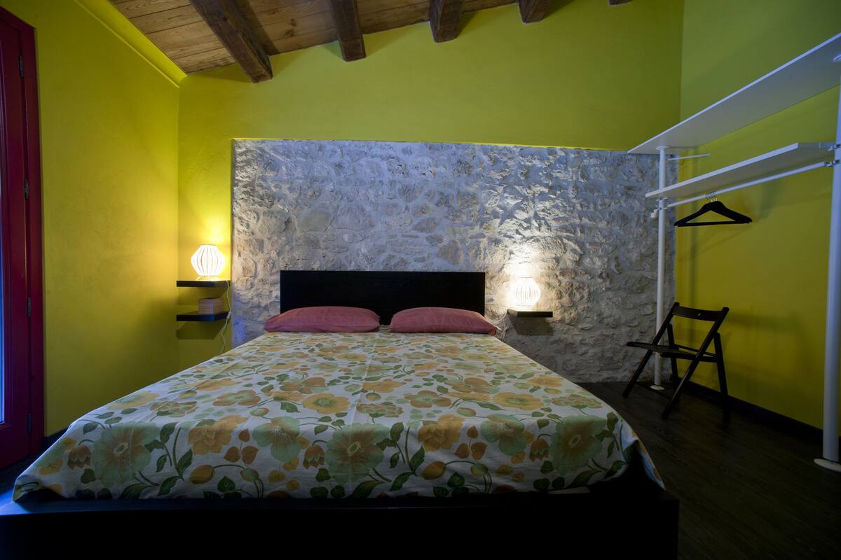 Una cama con colcha estampada con motivos florales, cabecera de piedra y dos lámparas de noche.