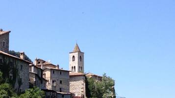 Un edificio storico in pietra con un campanile, circondato da un rigoglioso verde e alberi.