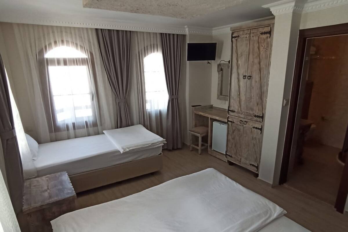 A hotel room with a large bed, a smaller bed, a desk, a wardrobe, and a TV.
