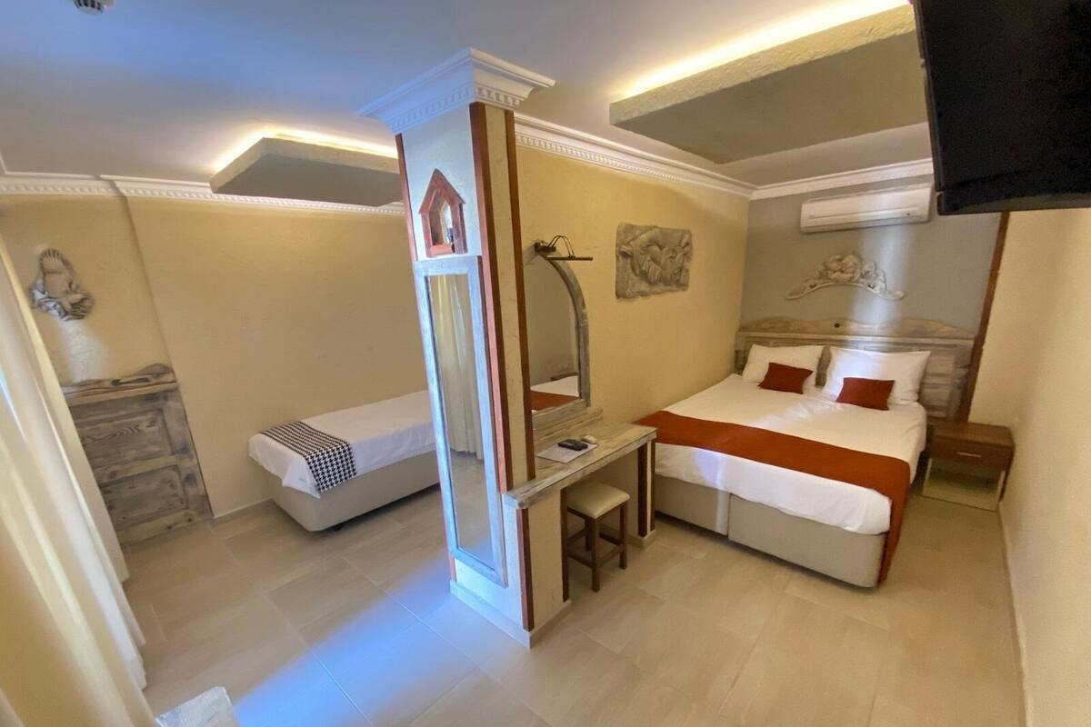 A hotel room with a bed, a desk, a chair, a mirror, and a small table.