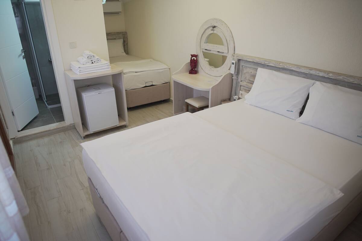 A hotel room with a large bed, a desk with a mirror, and a small bedside table.