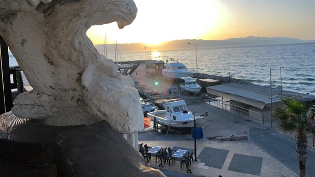 Un port de plaisance sur la côte, avec des bateaux amarrés, une promenade piétonne et un coucher de soleil en arrière-plan.