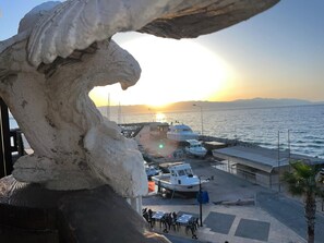 Un puerto costero con barcos amarrados, un paseo peatonal y un atardecer al fondo.
