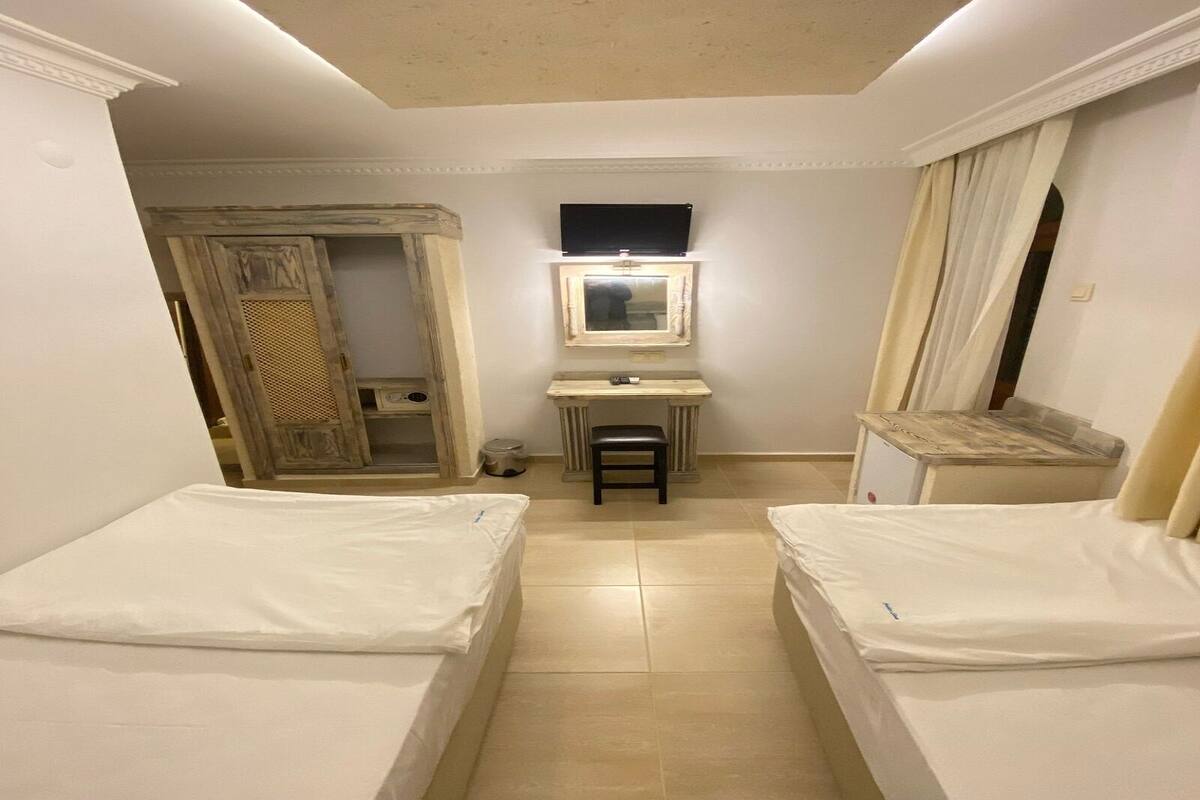 A small, well-lit room with two beds, a desk, and a wardrobe.