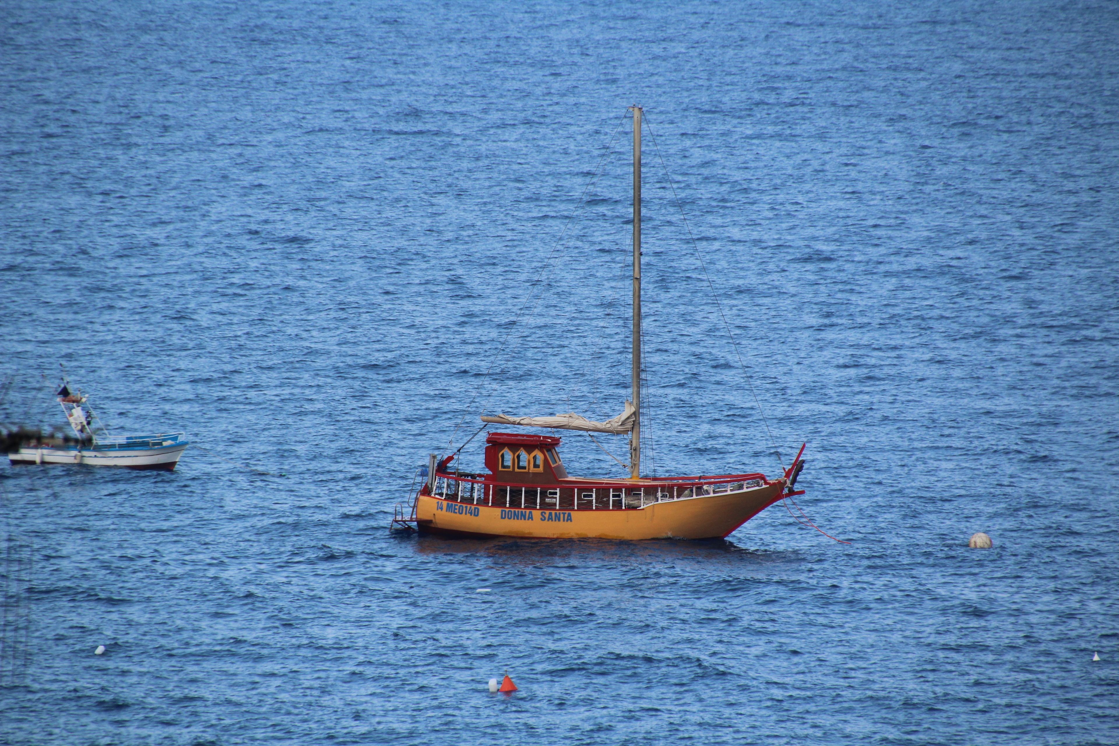 A small boat with a tall mast and a cabin, floating on calm water.
