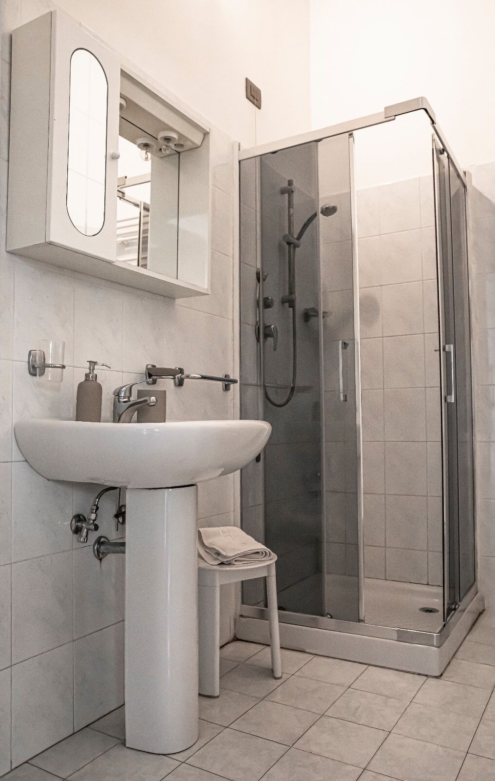 A modern bathroom with a white sink, mirror, and glass-enclosed shower.