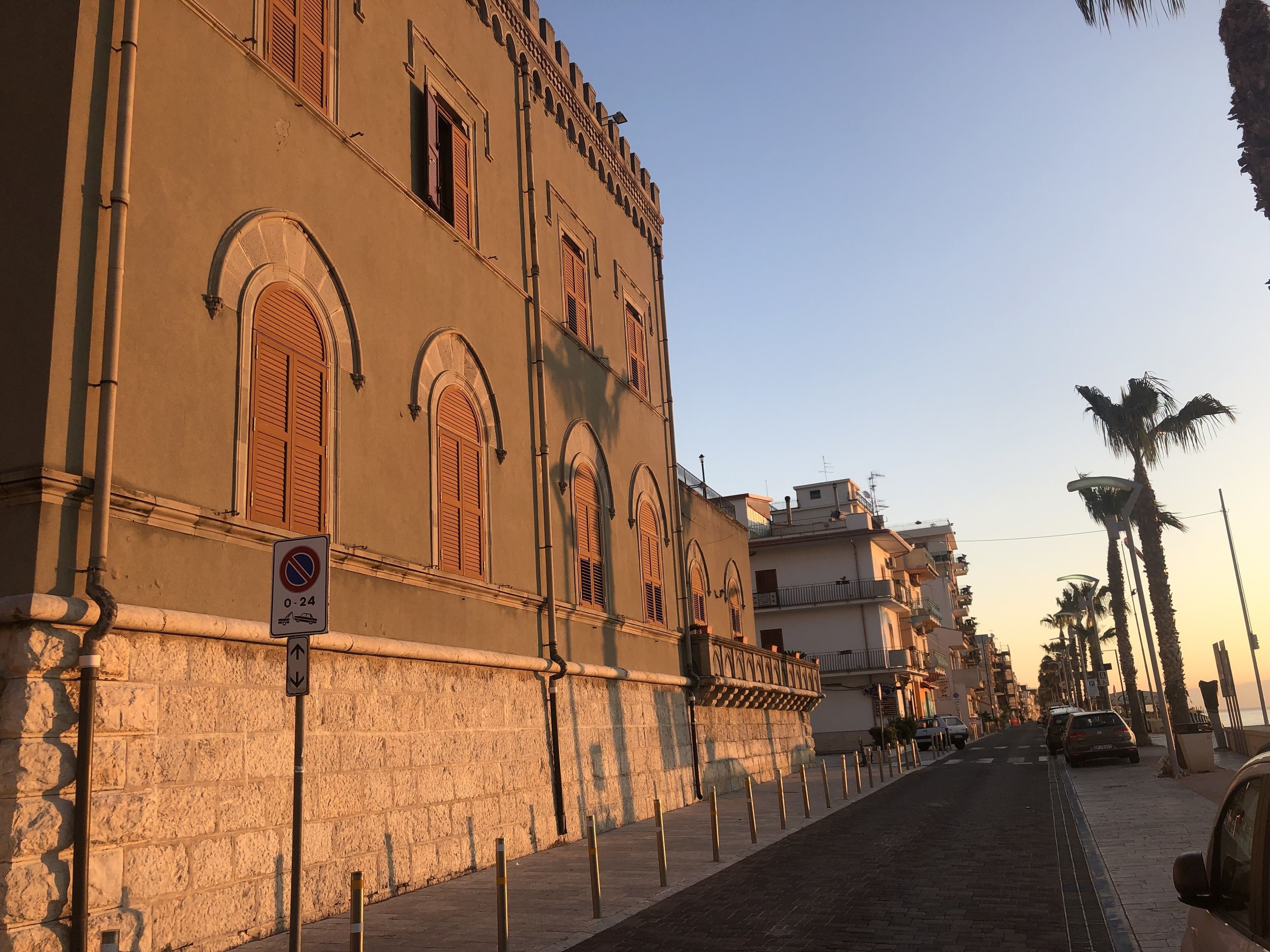 Una strada con un edificio storico caratterizzato da finestre ad arco e un divieto di sosta.