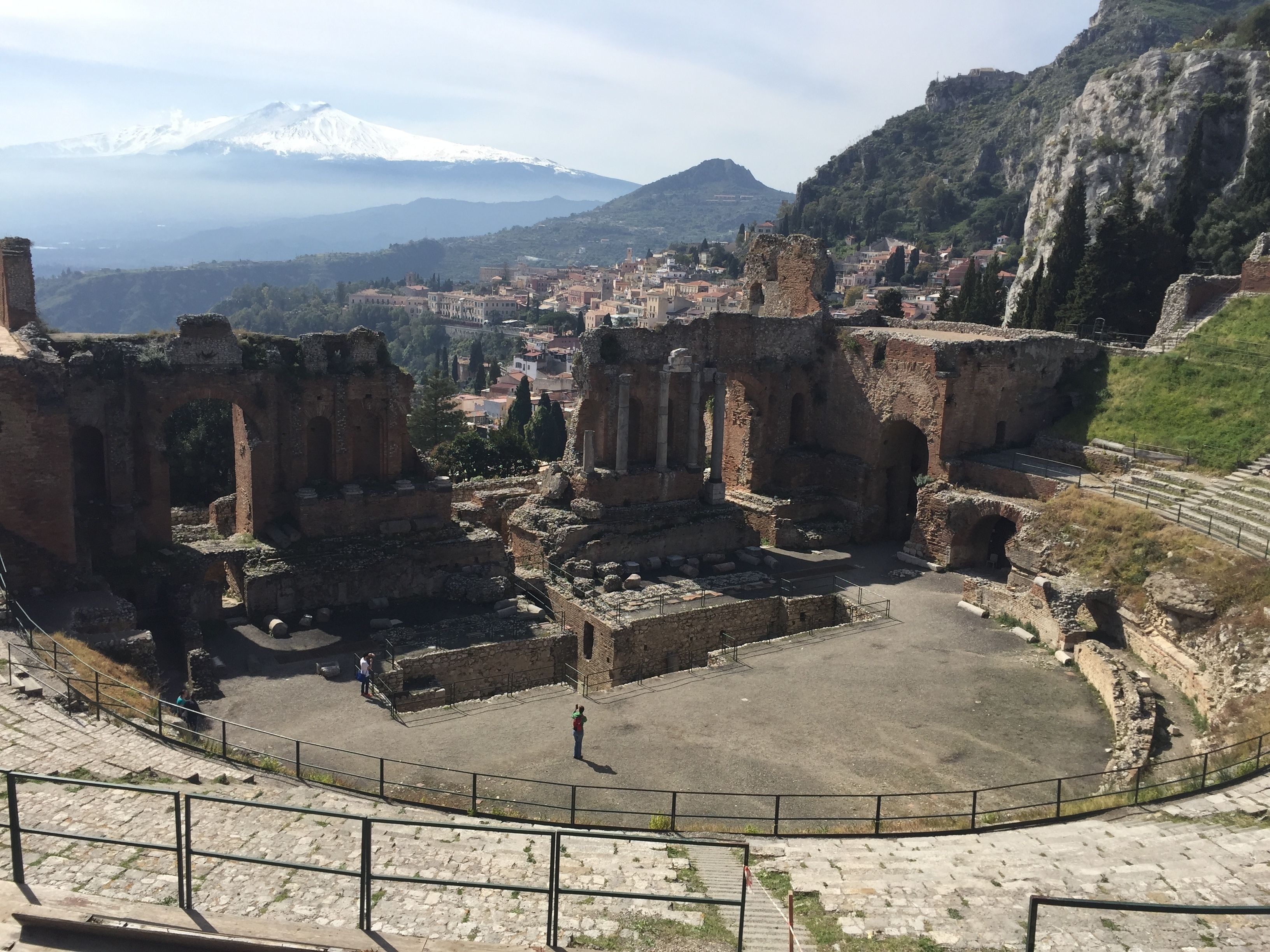 Ancient ruins with a central open area, stone steps, and a mountainous backdrop.