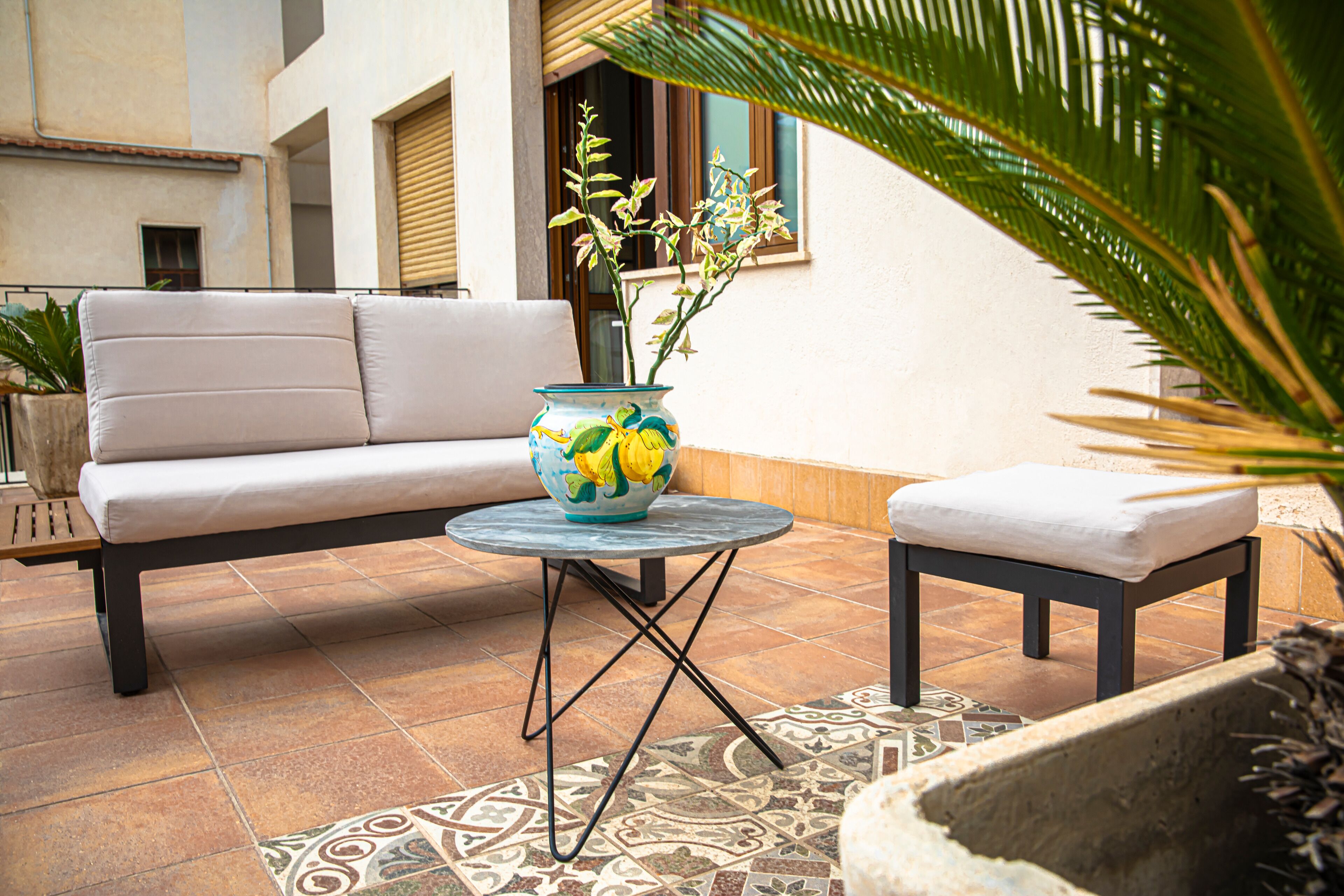 Une terrasse avec un canapé, une petite table et un vase décoratif.
