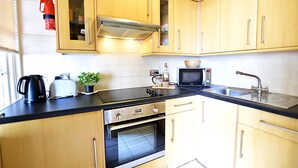 A compact kitchen with wooden cabinets, a microwave, a kettle, and a toaster.