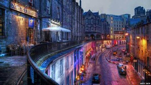 A historic street with a curved bridge, a pub named 'MAXIES', and traditional architecture.