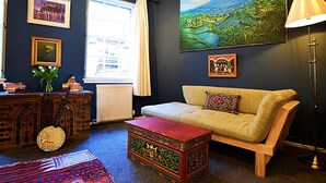 A cozy living room with a sofa, a coffee table, a lamp, a guitar, a radiator, and a painting of a landscape.