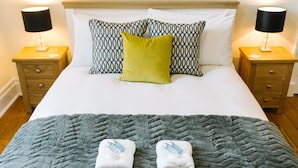 A neatly made bed with patterned pillows, a grey knitted blanket, and two folded towels on the bed. - JOIVY Great Location! Heart of City Centre 3bed Apartment (Edinburgh)