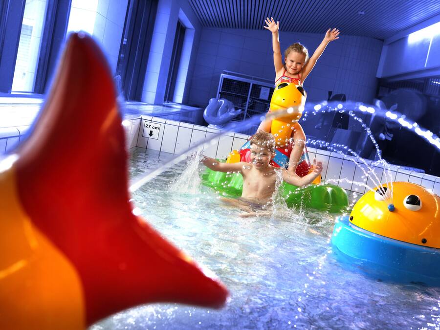 Ein Kind spielt in einer Wasserspielanlage mit aufblasbaren Spielsachen und einer Wasserrutsche.