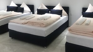 A hotel room with three beds, each with a black headboard and white bedding. The room has a tiled floor and a white wall. - Hotel Restaurant Memo (Mannheim)