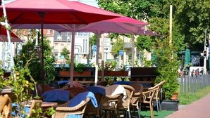 Outdoor seating with umbrellas, a paved walkway, and a view of buildings in the background. - Hotel Restaurant Memo (Mannheim)