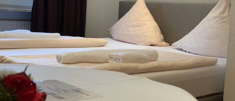 A hotel room with two beds, each with white linens and pillows, a small potted plant, and a window with curtains.