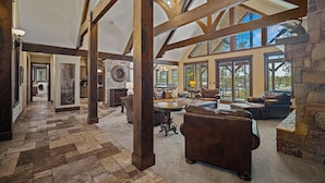 A spacious living area with high ceilings and exposed wooden beams, featuring a stone fireplace, leather sofas, and a large dining table. - Trailmere Escape with Access to Forest House (Bend)