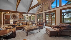 A spacious living room with leather furniture, a stone fireplace, and large windows offering views of the outdoors. - Trailmere Escape with Access to Forest House (Bend)
