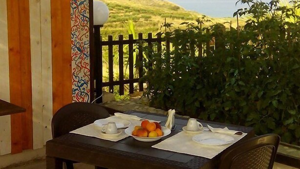 A table set for two with a view of the sea, a wooden wall with a colorful pattern, and a black metal fence. - Casa Vacanza Villa Sole (Siculiana)