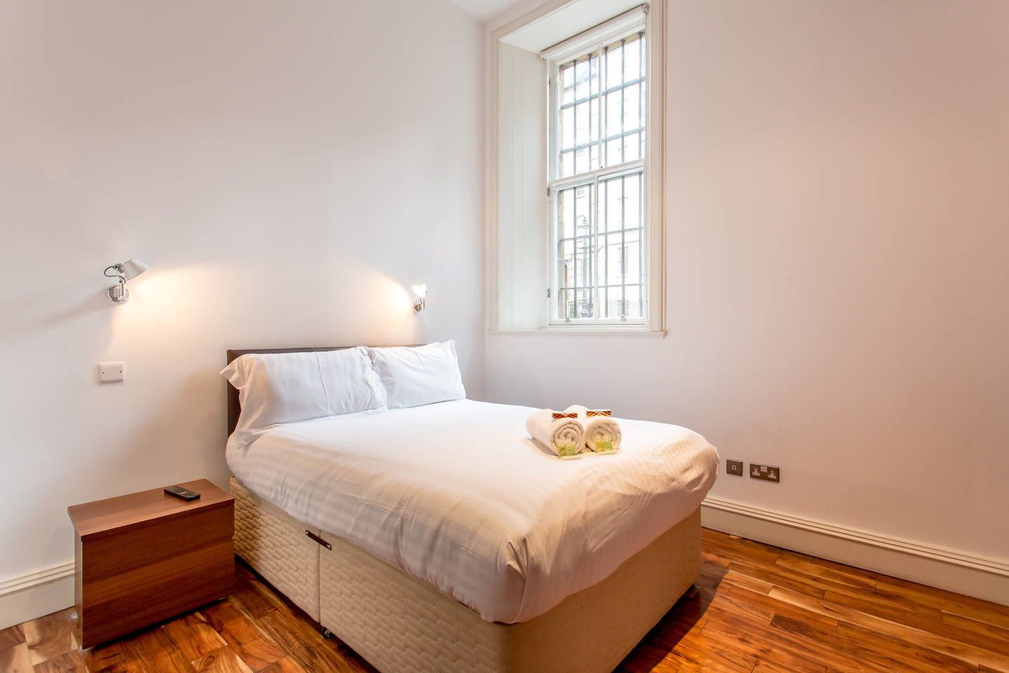 Un dormitorio con cama, mesita de noche, lámpara y ventana.