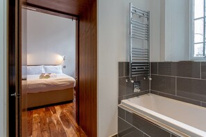 A modern bathroom with a large bathtub, a towel rack, and a wooden floor. - JOIVY Location, Location! North Bank Street Luxury Apt (Edinburgh)