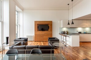 A modern living room with a glass dining table, black leather sofas, and a TV mounted on a wooden wall. - JOIVY Location, Location! North Bank Street Luxury Apt (Edinburgh)