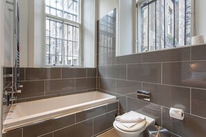 A modern bathroom with a bathtub, toilet, and large windows. - JOIVY Location, Location! North Bank Street Luxury Apt (Edinburgh)
