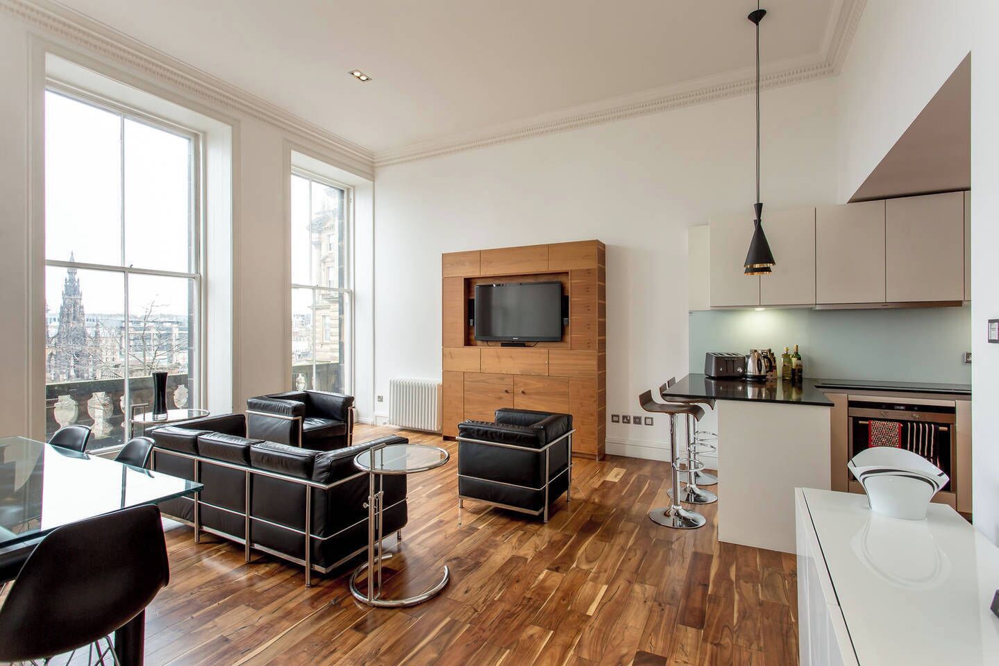 Eine moderne Wohnung mit Wohnbereich, Essplatz und Küche. Sie verfügt über große Fenster, einen Flachbildfernseher und Holzböden.