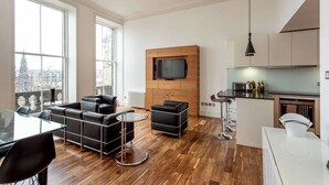 A modern apartment with a living area, dining space, and kitchen. It features large windows, a flat-screen TV, and wooden flooring. - JOIVY Location, Location! North Bank Street Luxury Apt (Edinburgh)