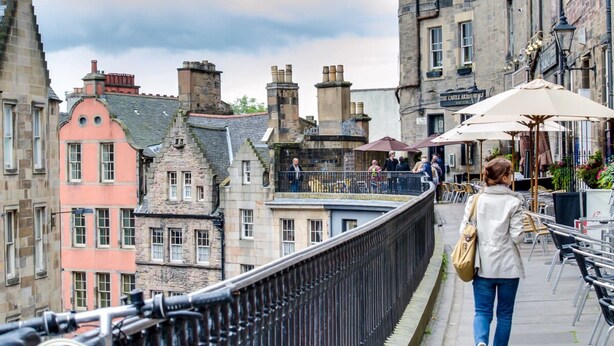 A pedestrian walkway with a metal railing, overlooking a street with buildings and outdoor seating areas. - JOIVY Location, Location! North Bank Street Luxury Apt (Edinburgh)