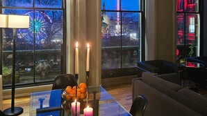 A dining area with a table set for four, two candles, and a view of a cityscape at dusk. - JOIVY Location, Location! North Bank Street Luxury Apt (Edinburgh)