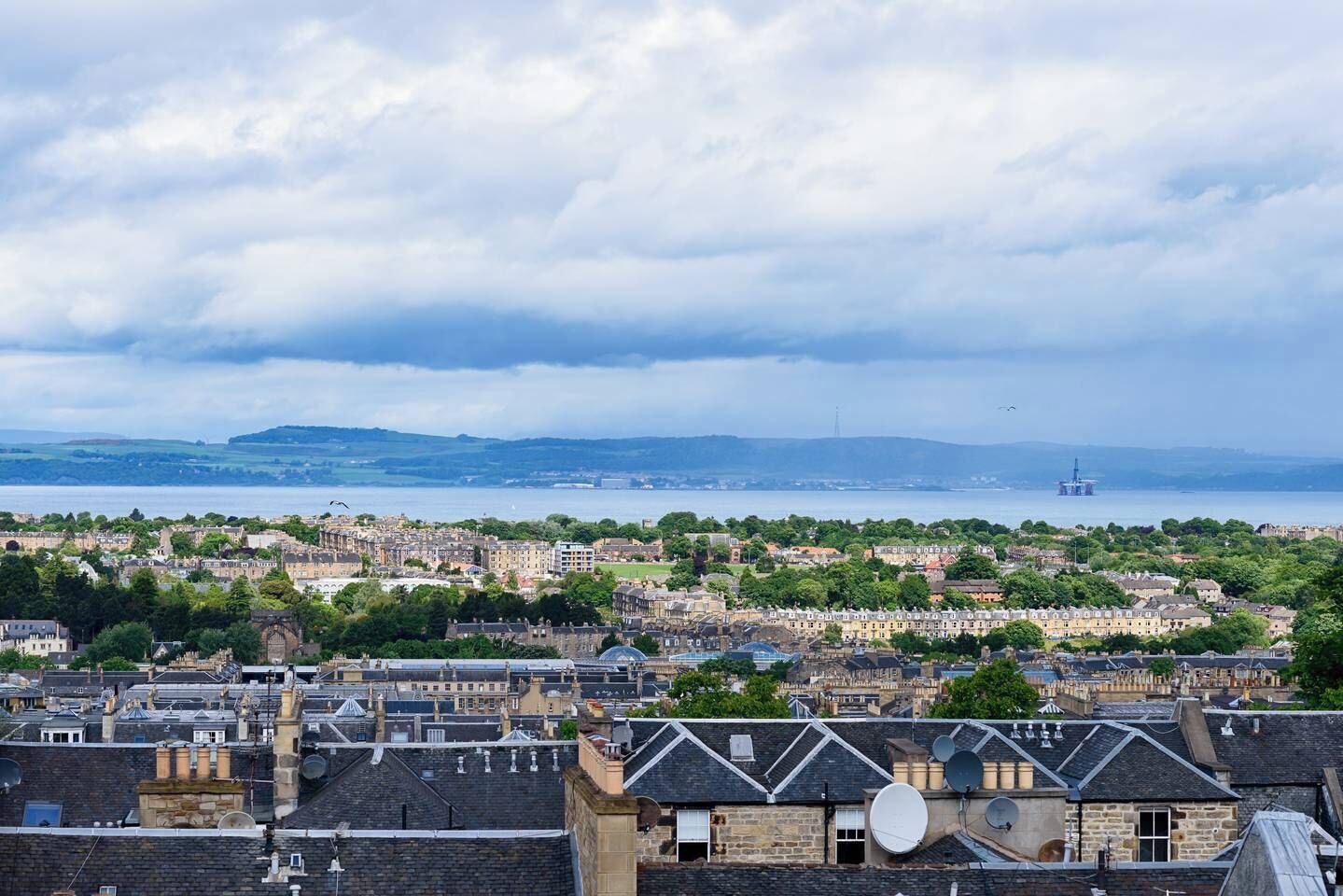 Un paisaje urbano costero con edificios históricos, un puerto y una plataforma petrolera distante.