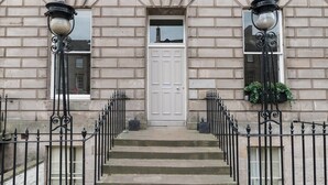 A building with a white door, two black wrought iron gates, and a set of stone steps leading to the entrance. - JOIVY York Place Apartment in Georgian City Centre Building (Edinburgh)